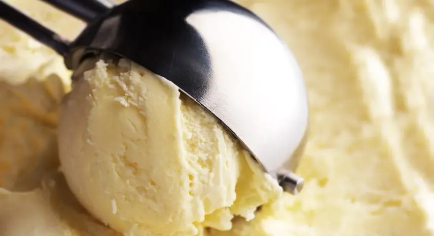 Un cucchiaio raccoglie una pallina di cremoso gelato con yogurt greco, pronto per essere gustato.