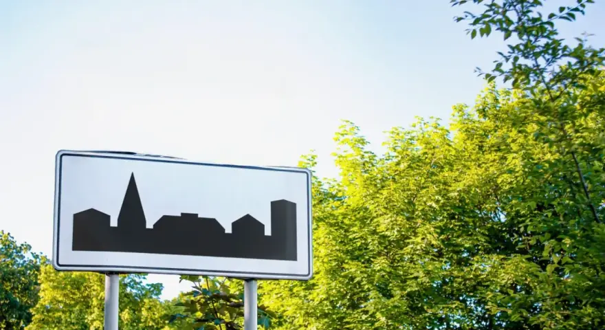 Znak informuje o wjeździe do obszaru zabudowanego. Sylwetka miasta na białym tle.