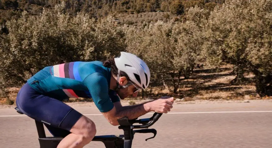 Cyclist pushing hard on a road bike, focused on a VO2 max workout amidst a scenic, tree-lined landscape.