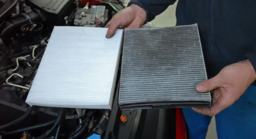 Hands hold a new white air filter next to a dirty, used one, ready to replace air filter in car.