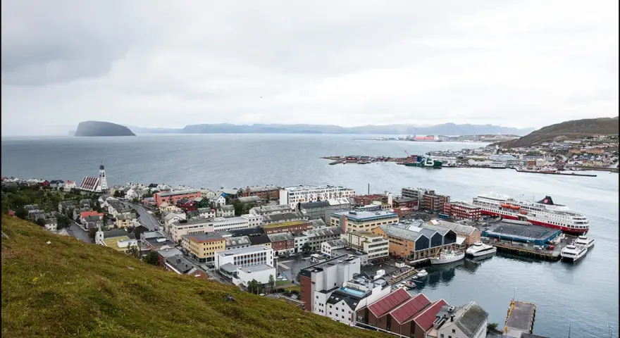 Vy över en stad vid havet med färjor vid kaj. En kyrka med högt torn syns i förgrunden. Detta är Norges nordligaste stad.