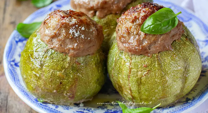 Zucchine tonde ripiene, un piatto gustoso del menù di Benedetta, servite su un piatto blu e bianco con basilico fresco.