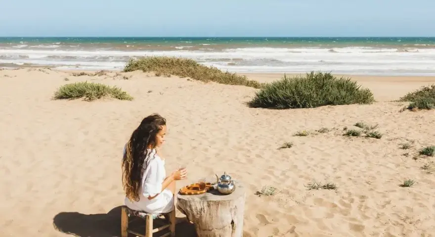 Kobieta pije herbatę na plaży, delektując się widokiem na wzburzone morze. To właśnie takie morze można podziwiać w Tunezji.