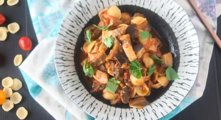 Orecchiette con pesce spada e melanzane, un piatto saporito e colorato, guarnito con basilico fresco.