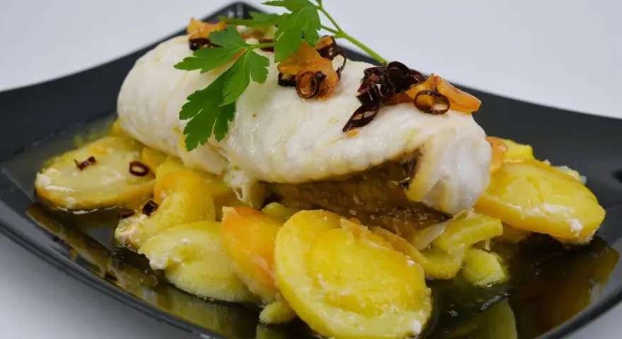 Rape con patatas, un plato delicioso con pescado blanco tierno y patatas doradas, decorado con perejil fresco y crujientes trozos de ajo frito.