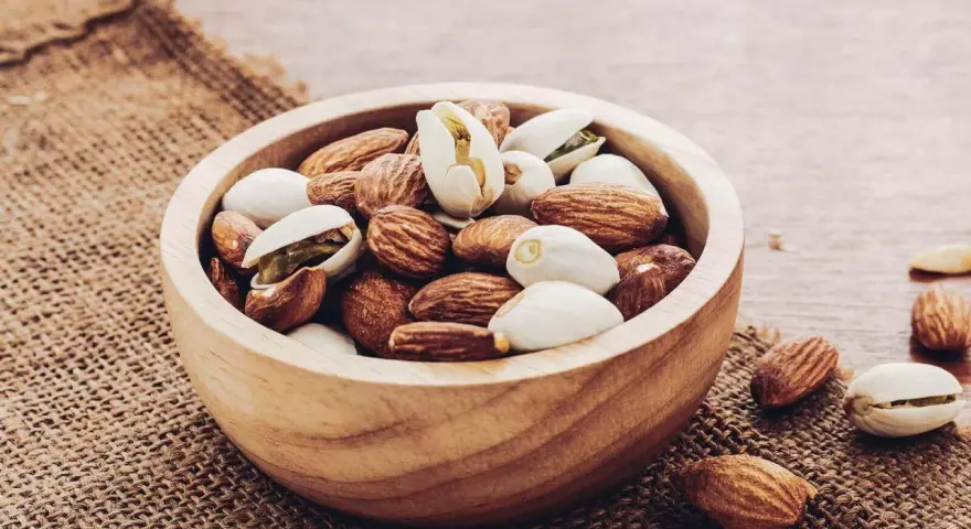 Un bol en bois rempli d'amandes et de pistaches, une liste d'oléagineux parfaite pour une collation saine.