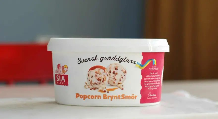 En burk SIA gräddglass med smak av popcorn och brynt smör. Glasskulor med kolasås och popcorn syns på etiketten.
