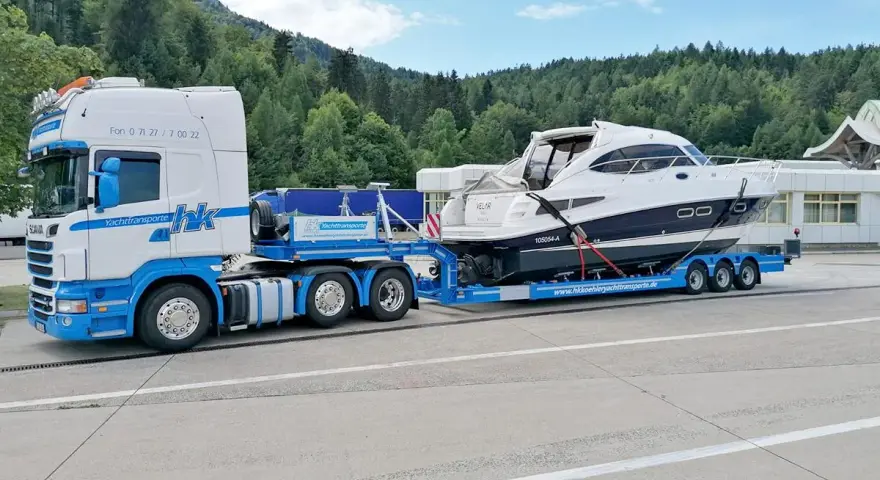 Ein LKW transportiert ein luxuriöses Boot auf einem Spezialanhänger. Die Yacht ist sicher auf dem Anhänger befestigt, bereit für den Transport über Land.