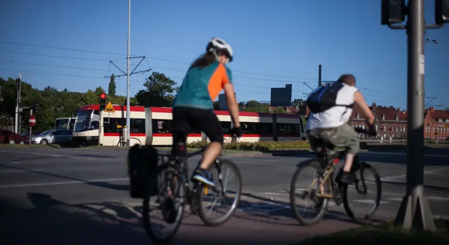 Rowerzyści jadący wzdłuż torów tramwajowych, w tle czerwono-biały tramwaj. Trasa rowerowa wiodąca w kierunku Westerplatte.