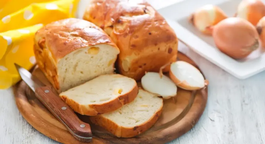 Zwiebelbrot rezept: goldbraune Brote mit Zwiebeln, angeschnitten, daneben Zwiebeln und ein Messer.