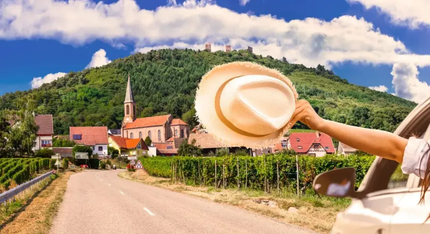 En bilresa längs den tyska rivieran, med en hatt som vinkar i vinden. En pittoresk by med en kyrka och vingårdar i bakgrunden.