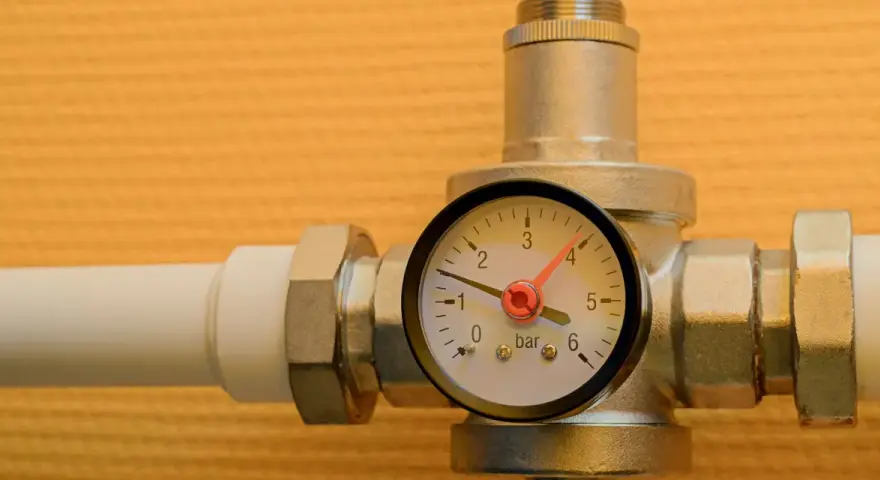 Un réducteur de pression d'eau avec un manomètre indiquant 1 bar. L'appareil est monté sur un tuyau blanc.