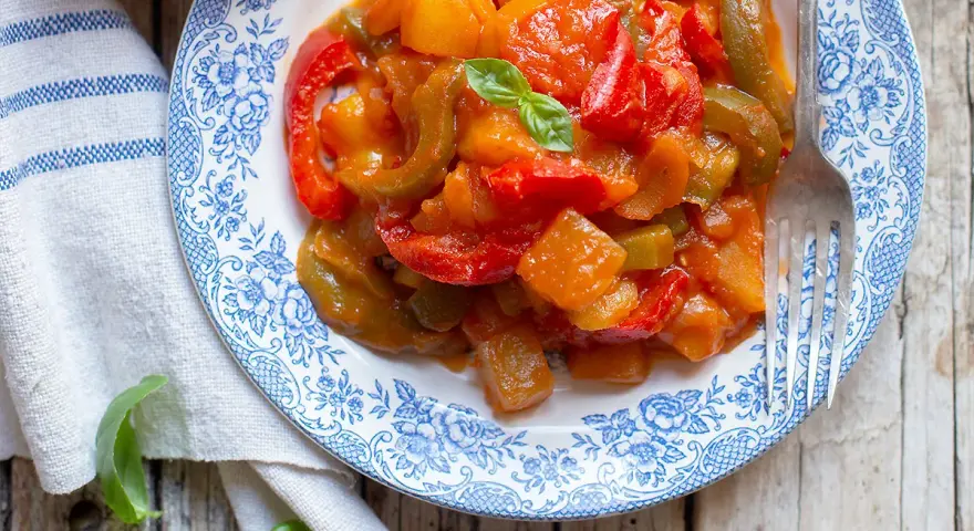 Un piatto di peperonata con patate, colorata e saporita, guarnita con basilico fresco.