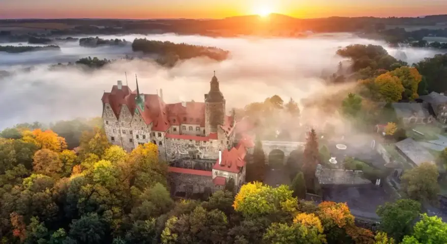 Zamek Czocha, gdzie jest, otoczony jesiennymi drzewami i mgłą o wschodzie słońca.
