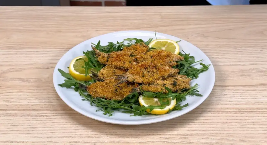Piatto di alici al forno dorate e croccanti, servite su un letto di rucola fresca con spicchi di limone.