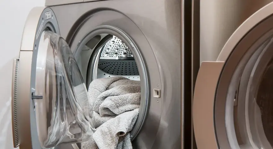 Eine offene Waschmaschine mit einem grauen Handtuch darin. Die Tür ist leicht geöffnet, um die Wäsche nach dem Waschen trocknen zu lassen.