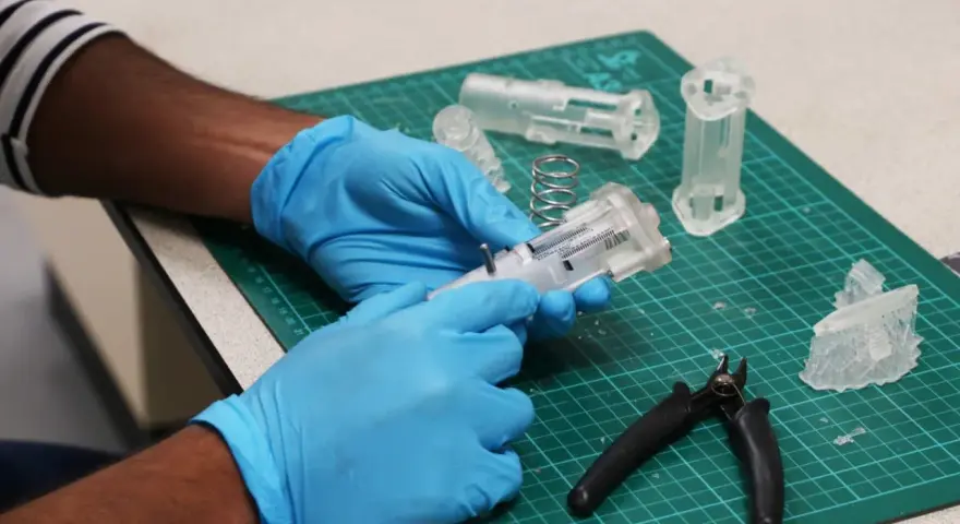 Hands in blue gloves assemble a 3D printed medical device prototype, showcasing innovation in healthcare technology.