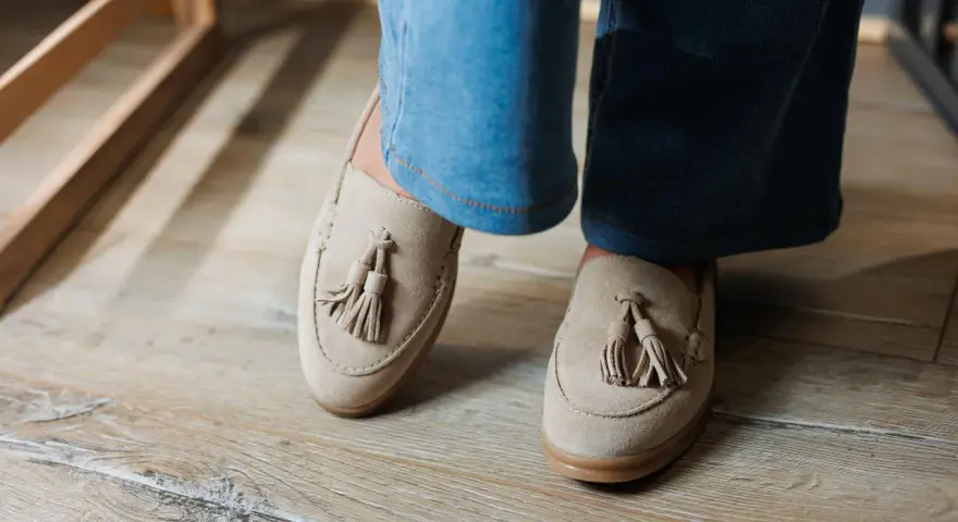 Beżowe mokasyny z frędzlami na drewnianej podłodze. Urocze stupki w casualowym stylu.