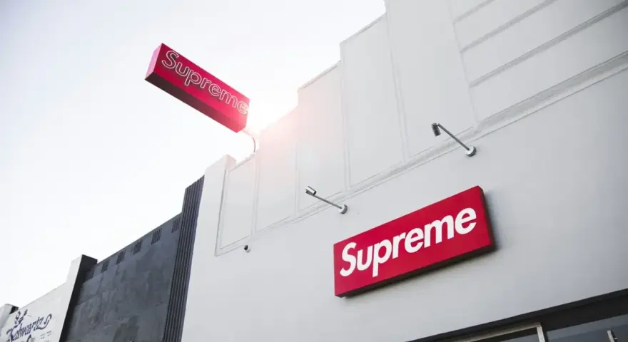 Znak Supreme na białej fasadzie budynku. Supreme to marka znana z limitowanych kolekcji streetwear.