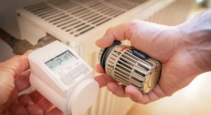 Hände tauschen ein sehr altes Thermostat gegen ein modernes Gerät an einem Heizkörper.