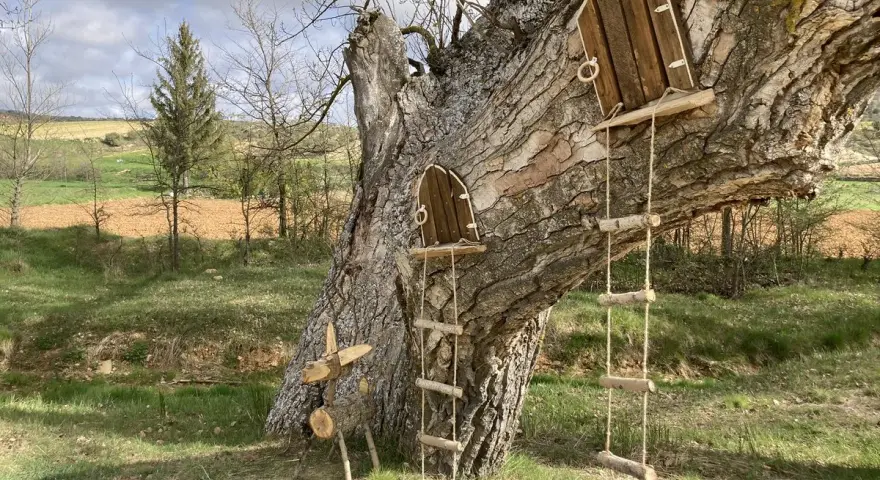 Un árbol con dos pequeñas puertas de madera y escaleras de cuerda, invitando a un arbolón paseo mágico. Un ciervo de madera decora la base.