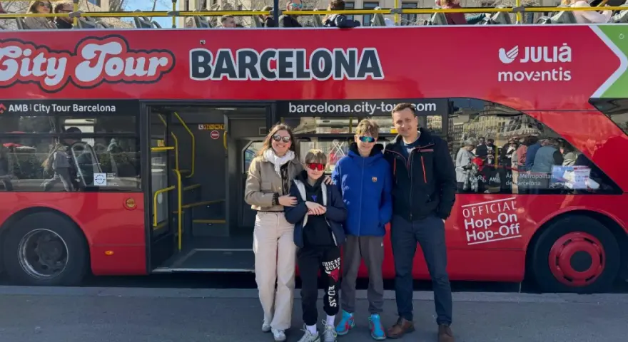 Family posing in front of a red "City Tour Barcelona" bus, ready for an adventure.