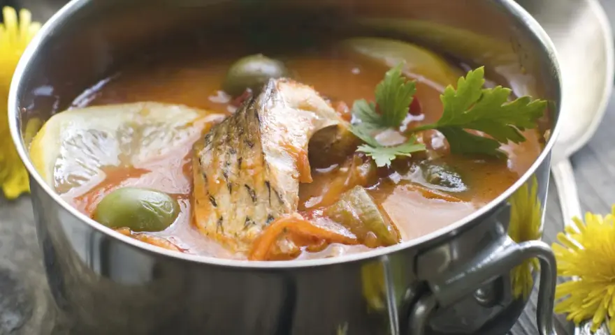 Aromaticzna rosyjska zupa rybna w metalowej misce, z kawałkami ryby, oliwkami, cytryną i natką pietruszki.