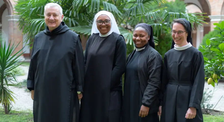 Four individuals in Benedictine habit smile in a garden.
