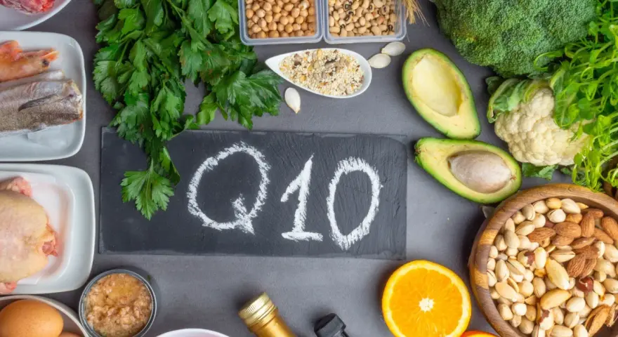 Q10 na tablicy, otoczone produktami bogatymi w koenzym Q10. Warto pamiętać o przeciwwskazaniach przy suplementacji.