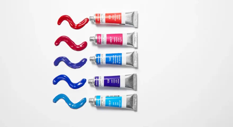 Des tubes de gouache Caran d'Ache rouge, magenta, bleu outremer, violet et cyan, avec des coulées de peinture sur fond blanc. Quelle peinture pour toile ?