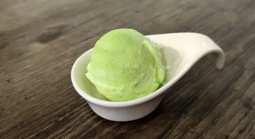 Una bola de helado de manzana verde brillante en una taza blanca sobre una mesa de madera.