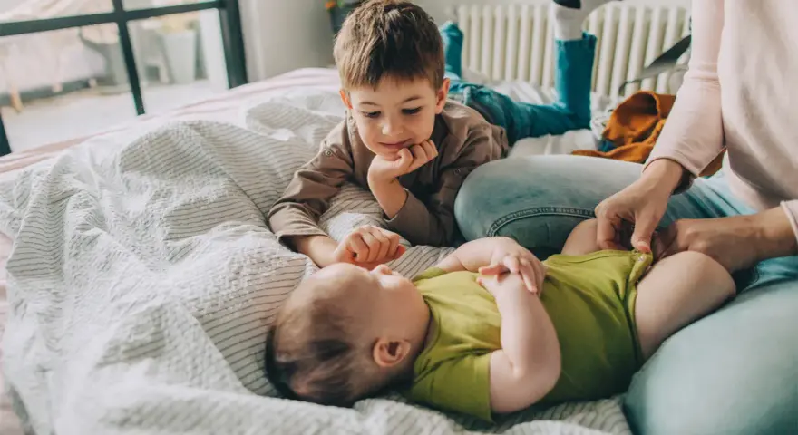Starszy brat patrzy z czułością na niemowlę, zastanawiając się, ile niemowlę rośnie w miesiąc.