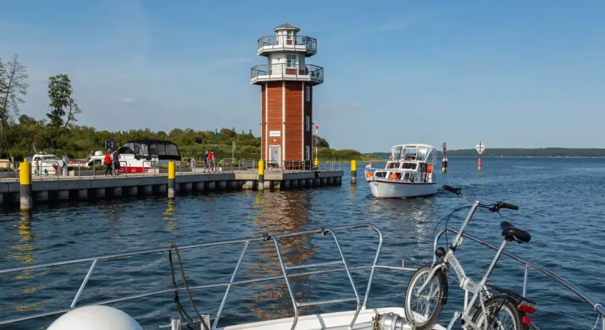 Plau am See: Leuchtturm und Promenade mit Booten. Ein Fahrrad wartet auf dem Vorderdeck.