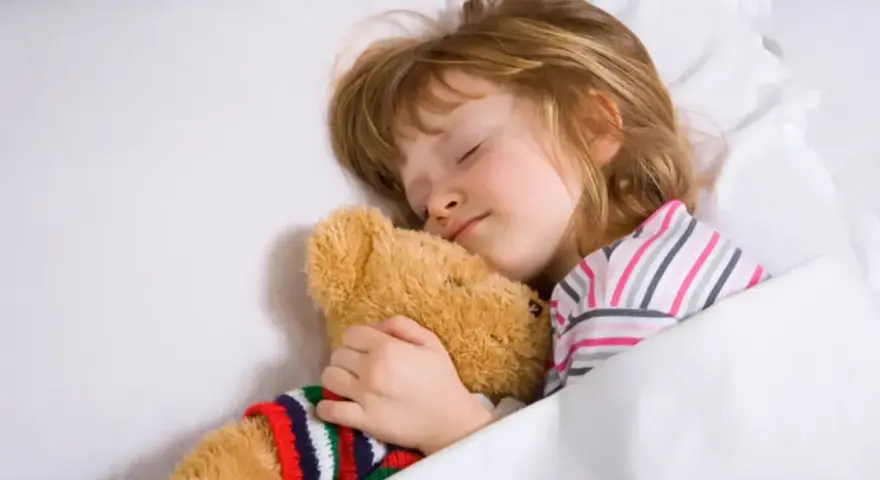Dziecko śpi wtulone w misia, w głębokim śnie, być może w fazie REM, marząc o przygodach.