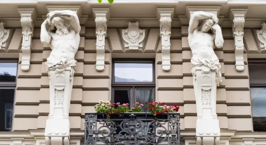 Dwie rzeźby atlantesów podtrzymujące balkon, przykład secesji w sztuce, zdobią fasadę kamienicy.