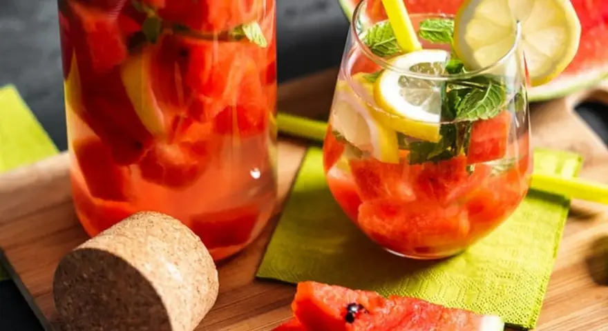 Orzeźwiający drink w arbuzie z cytryną i miętą, podany w szklance i karafce. Idealny na upalne dni.