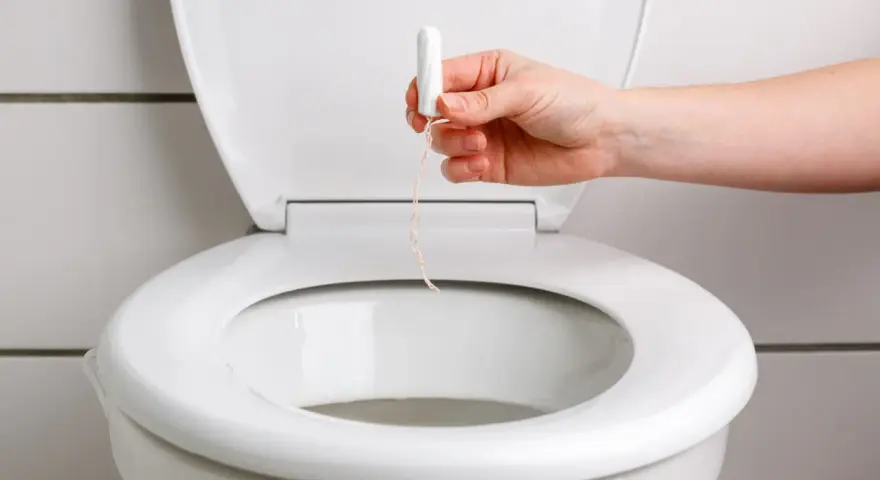 En hand håller en tampong över en toalettstol. Detta kan leda till stopp i toan.