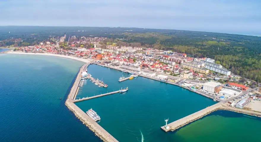 Widok z lotu ptaka na malowniczy hel port z licznymi łodziami i statkami. W tle rozciąga się miasto i las.
