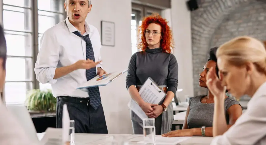 Un homme présente un rapport du liquidateur à une équipe. Une femme aux cheveux roux écoute attentivement.