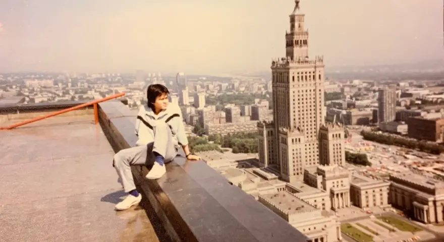 Młody mężczyzna siedzi na dachu, patrząc na panoramę Warszawy. W tle Pałac Kultury i Nauki, który wtedy był najwyższym budynkiem, zanim powstał Marriott.