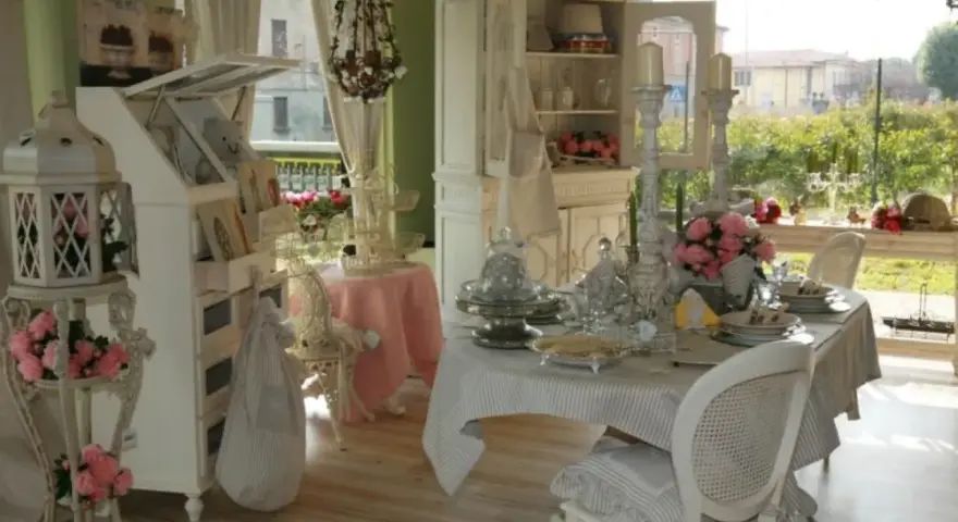 Un tavolo apparecchiato in **stile provenzale francese**, con sedie bianche, candelabri e fiori rosa.