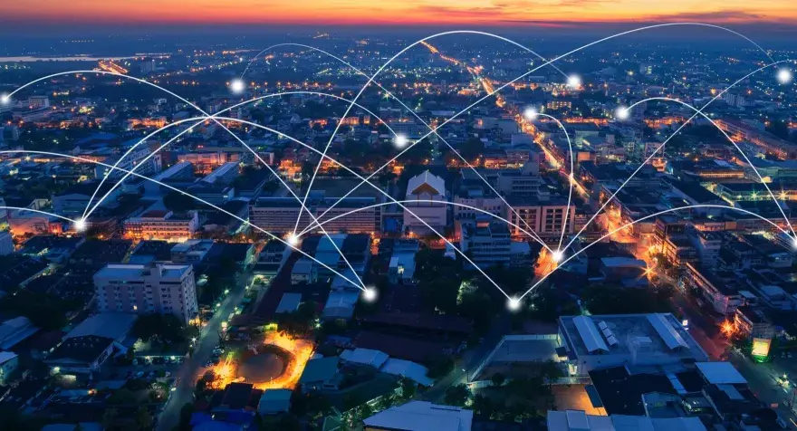 Aerial view of a city at dusk, with glowing lines connecting buildings, symbolizing modern infrastructure and networking.