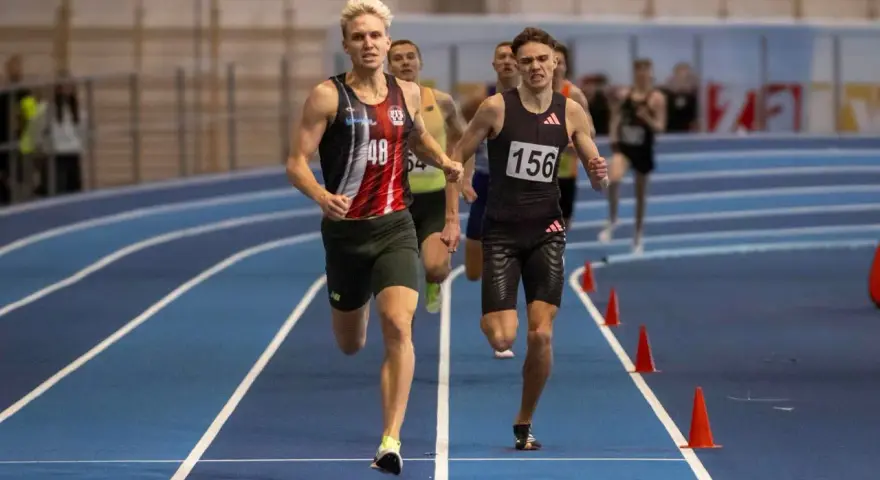 Filip Ostrowski biegnie w zawodach lekkoatletycznych. Dwóch zawodników na pierwszym planie, jeden z numerem 48, drugi z 156.