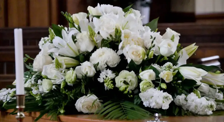 Un arreglo floral blanco sobre un ataúd, con lirios, rosas y otras flores. Estas flores para difuntos simbolizan paz y pureza en el adiós.