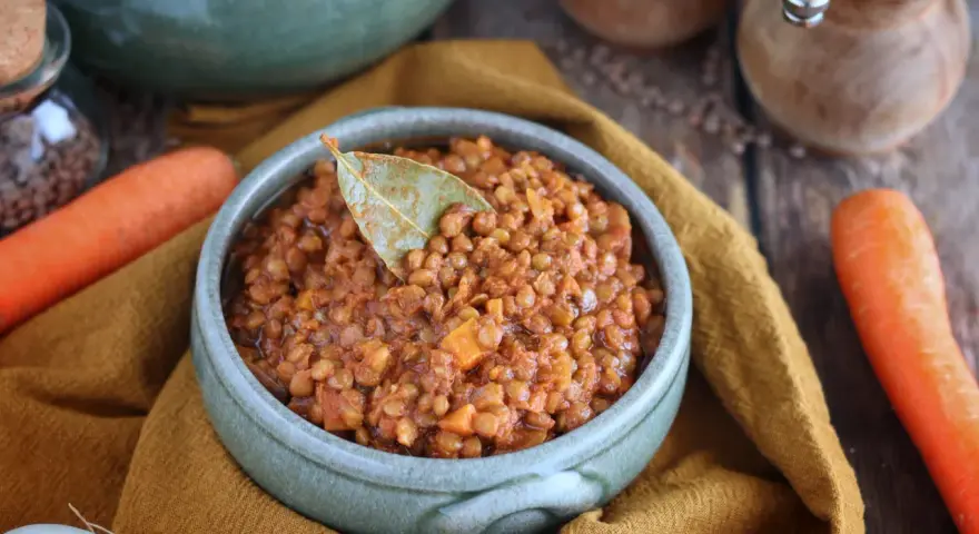 Un invitante ragù di lenticchie, profumato con alloro, pronto per essere gustato. Accanto, carote fresche e cipolla.