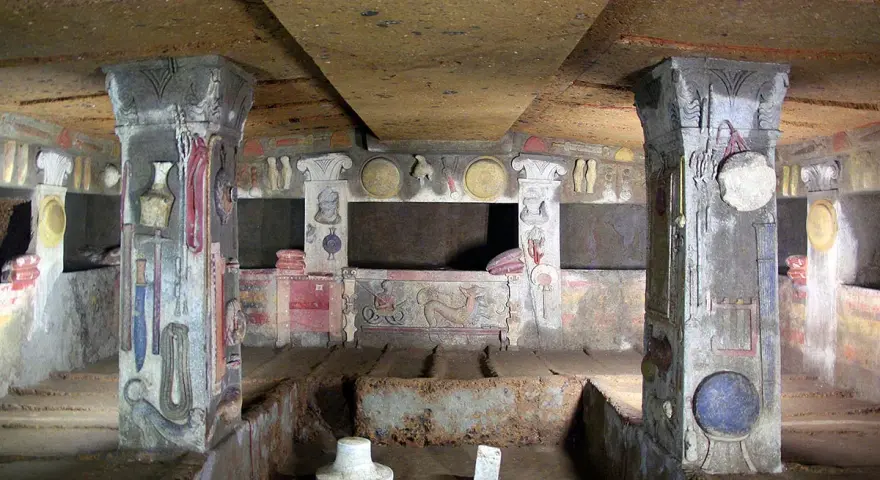 Inside a tomb at the Cerveteri Necropolis, painted columns and walls depict ancient life.