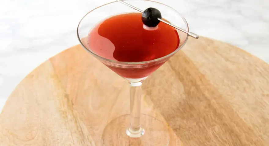 Czerwony drink w kieliszku koktajlowym, ozdobiony oliwką na wykałaczce. Idealny drink San Francisco na letnie wieczory.