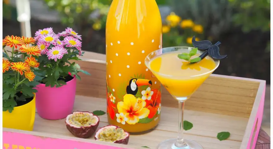 Tropische Früchte und ein leuchtend gelber Drink auf einer rosa Holzschale. Ein ideales Solero Schnaps Rezept ohne Sahne für heiße Tage.