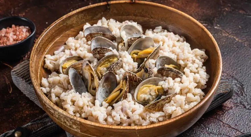 Un tazón de madera lleno de arroz cremoso y almejas frescas, un plato delicioso de arroz con almejas.