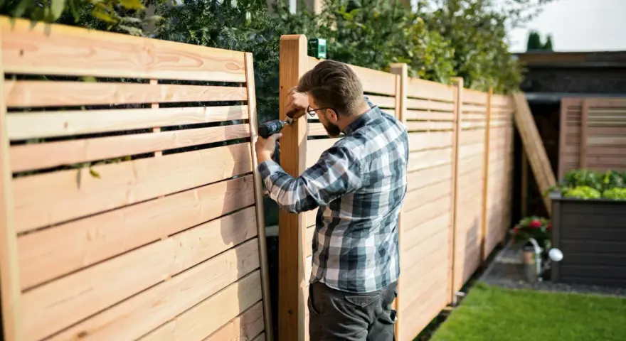 Uomo con trapano realizza una staccionata in legno fai da te, creando un'elegante divisione per il giardino.